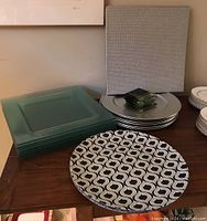 Overall view of all items including green plastic charger plates, clear square glass chargers, and glass coasters stacked on a wooden table.