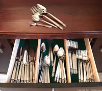 Photo of open wooden flatware drawer showing knives, forks, spoons, teaspoons, and dessert forks with decorative handles.