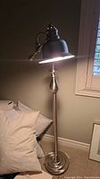 Floor lamp shown lit from a front angle, showing overall design and lighted metal shade.