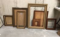 Seven various antique frames arranged on concrete floor showing style, color and scale