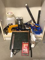 Wide view of all framing supplies including mat cutter, paper cutter, rulers, staple gun, wire spools, stapler, tape, and tools in blue tray.