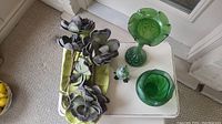 Overview of lot contents on white table showing green marbled glass vase, rose bowl, glass perfume bottle on stand, faux magnolias on leaf-shaped green platter