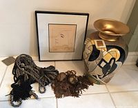 Overall view of framed print, Picasso vase, and two tassels on rope laid out on tiled surface.