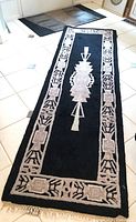 Top down view of black Deco pattern wool runner with beige geometric design, showing full length and fringed end.