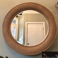 Front view showing round beveled mirror with textured ridged frame reflecting room interior.