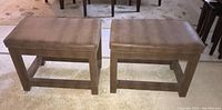 Pair of rectangular wood framed stools with padded seats covered in brown vinyl with faux reptile texture, positioned side by side on a carpeted floor.