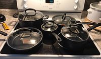 Full set of T-Fal cookware on stove showing three pots and two fry pans all with glass lids and black handles.