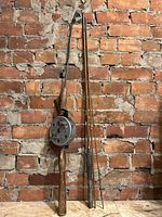 Photo of two antique fishing rods leaning against a brick wall: trolling rod with reel on left, bamboo fly rod on right