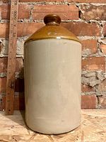Full frontal view of the large ceramic jug showing size reference with ruler beside it against a brick background.