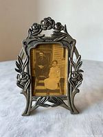 Front view of pewter Art Nouveau picture frame holding vintage portrait photo. Shows detailed floral and leaf decorations on all sides of frame.