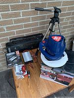 Full lot view showing all items on wood surface against brick background including boom box, buffer, inverter with cables, and tripod