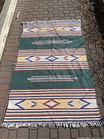 Full view of the cotton woven rug laid flat on a brick surface showing the full pattern and color scheme.