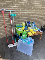 Large assortment of cleaning supplies including mops, gloves, cleaning chemicals, gloves, and plastic container with supplies.
