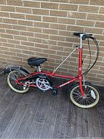 Full side view of red folding bike against brick wall