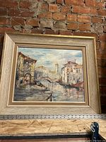 Full view of framed oil painting in mid-century modern style frame against brick wall.