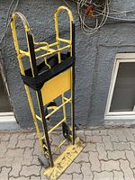 Full view of the yellow appliance movers dolly showing the frame, handles and base plate with signs of heavy use and paint wear.