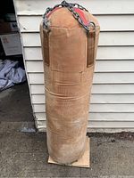 Full view of heavy-duty punching bag with brown corduroy fabric, standing upright on a wooden base support, showing overall condition and detail.