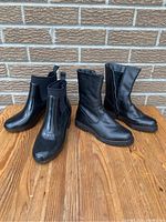 Four pairs of ladies black boots arranged on a wooden surface against a brick wall background