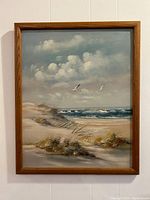 Full view of the framed painting showing sea waves, sand dunes, grass, and flying gulls with clouds above.