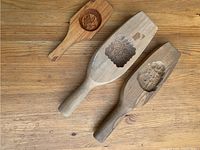 Three carved wooden molds laid on wooden surface showing detailed relief designs: floral motif, flower with scalloped border, and Buddha figure.