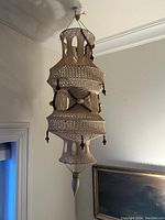 Photo of large white macrame hanging shade sculpture with wooden bead embellishments, suspended from ceiling, showing intricate handwoven details and shape suitable for LED lighting.