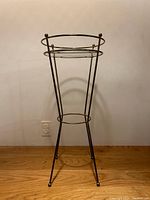 Full view of metal atomic style plant stand with three legs and top circular rim with spherical finials.