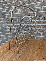 Front angled view of the Mid Century Modern magazine rack showing the V-shaped metal wire lines and woven handle detail.
