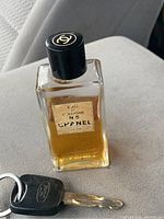 Closed vintage Chanel No.5 rectangular glass perfume bottle with black screw cap and partial amber liquid contents inside.