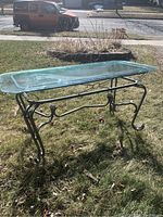 Full view of the wrought iron occasion table with glass top standing outdoors on grass, showcasing the overall structure and condition.