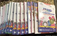 Fourteen packs of Prang medium weight construction paper, stacked in original packaging showing colorful design and branding.
