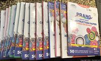 14 packages of Prang medium weight construction paper stacked side by side showing packaging and quantity.