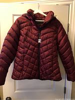 Front view of the women's burgundy puffer jacket hanging on a hanger, showing quilted chevron pattern and zipper.