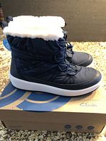 Side profile of navy women's boots on box showing white faux fur cuff and thick sole