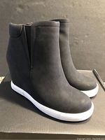 Pair of Kenneth Cole Kam black wedge sneakers front and side view showing smooth black upper, white sole and wedge heel.