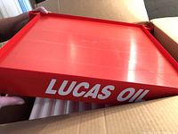 Close-up of red Lucas Oil branded plastic shelf tray showing logo and tray design with raised edges.