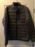 Front view of the grey men's Starter StormStar jacket hanging on a door. Shows horizontal quilted design and zipper pockets.