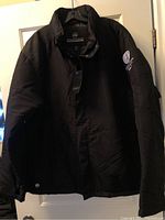Front view of mens black Stormtech jacket with tags, size 2XL, hanging on a hanger.