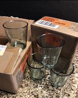 Four translucent grayish plastic cups displayed in front of unopened boxes with shipping labels on a granite countertop.