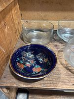 Blue ceramic bowl with floral and bird motifs alongside several clear glass bowls on wooden surface.