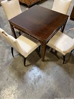 Photo of square wooden dining table with four upholstered cream fabric chairs