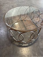 Round glass coffee table with decorative metal base on concrete flooring