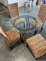 Full top view of the glass dining table surrounded by woven chairs, showing round glass surface and metal frame base.