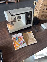Kenmore sewing machine powered on set on a wooden table with instruction manual and foot pedal.