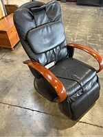 Side angle view of black leather massage chair with wooden armrests on concrete floor