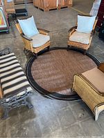 Three wicker chairs with beige cushions, a metal and wood bench with a striped cushion, and a round brown outdoor rug on concrete floor.