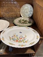 Serving platters on wooden shelf showing glass and ceramic pieces in various patterns.