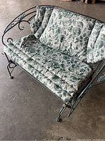 Front angle showing green metal porch bench with floral cushions on seat and backrest.