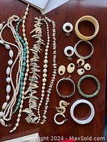 Photo showing multiple necklaces with ivory, stone, turquoise beads and several bracelets and earrings arranged on a wooden surface.
