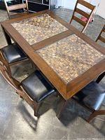 Angle showing wood dining table with two woven wicker or rattan inset panels under glass, surrounded by wooden chairs with black padded seats.