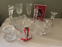 Eleven Waterford Crystal pieces arranged on a table: two golfer figurines, Madonna figurine, two crystal bowls, a creamer, a goblet, flute, candlestick, votive candleholder, and two Christmas ornaments (one in a red box).
